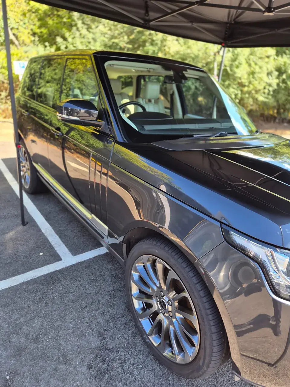 Black Range Rover with polished paint and chrome wheels under a canopy